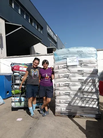 Two female volunteers next to a pallet of donated feed sacks